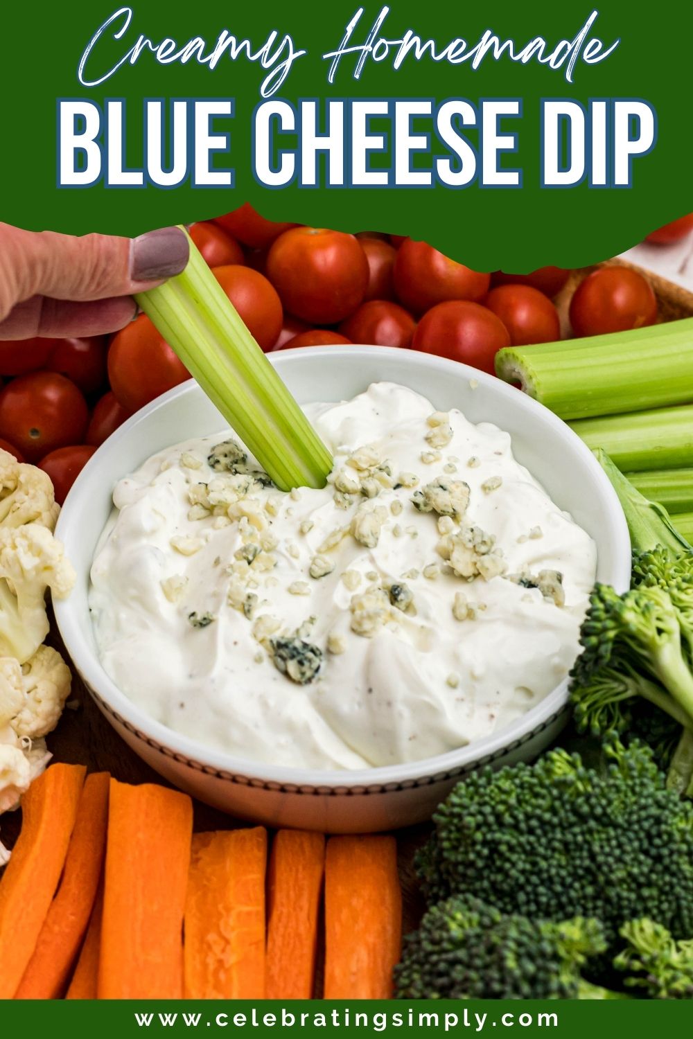 Round white bowl filled with blue cheese dip, surrounded by veggies, with a piece of celery being dipped into center.