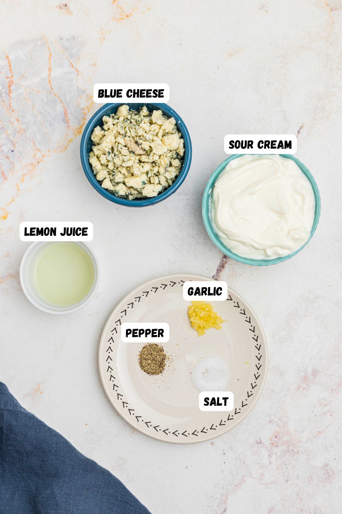 Sour cream, blue cheese, lemon juice, and seasonings, in small bowls and labeled on a marble table. 