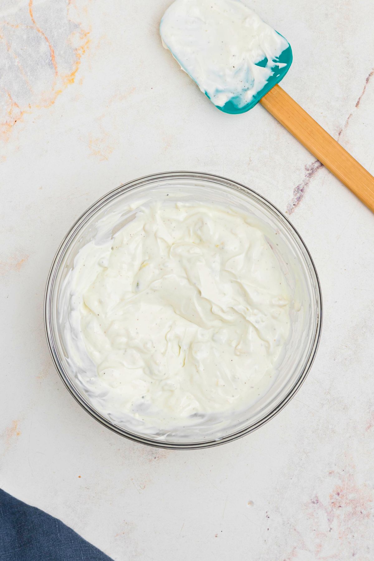 Clear glass bowl with dip  after being mixed together, with spatula on the table. 
