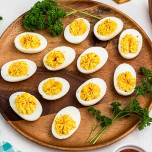 Bright white and yellow deviled eggs, sliced in half, on a round wooden serving platter with parsley garnish.