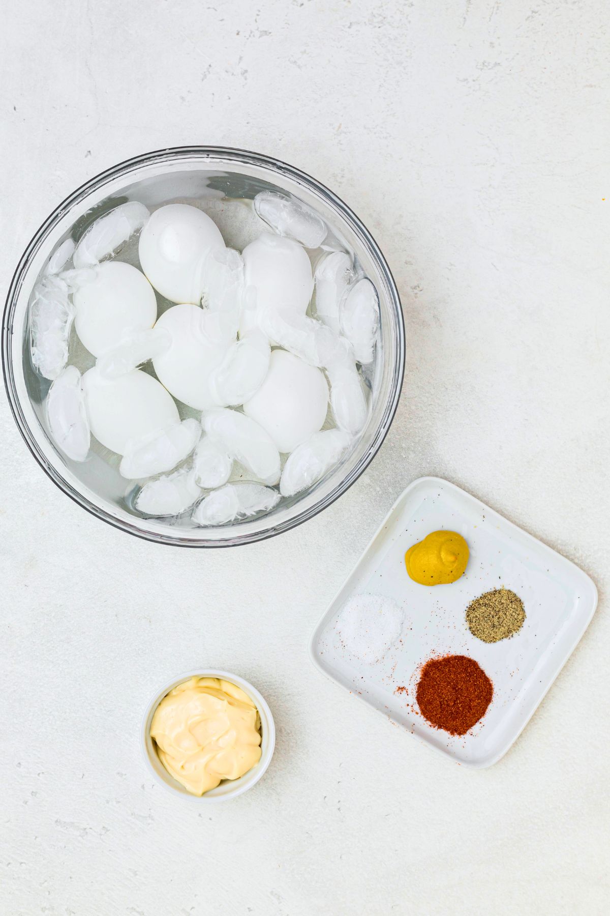 Boiled eggs in a clear glass bowl, filled with water and ice. 