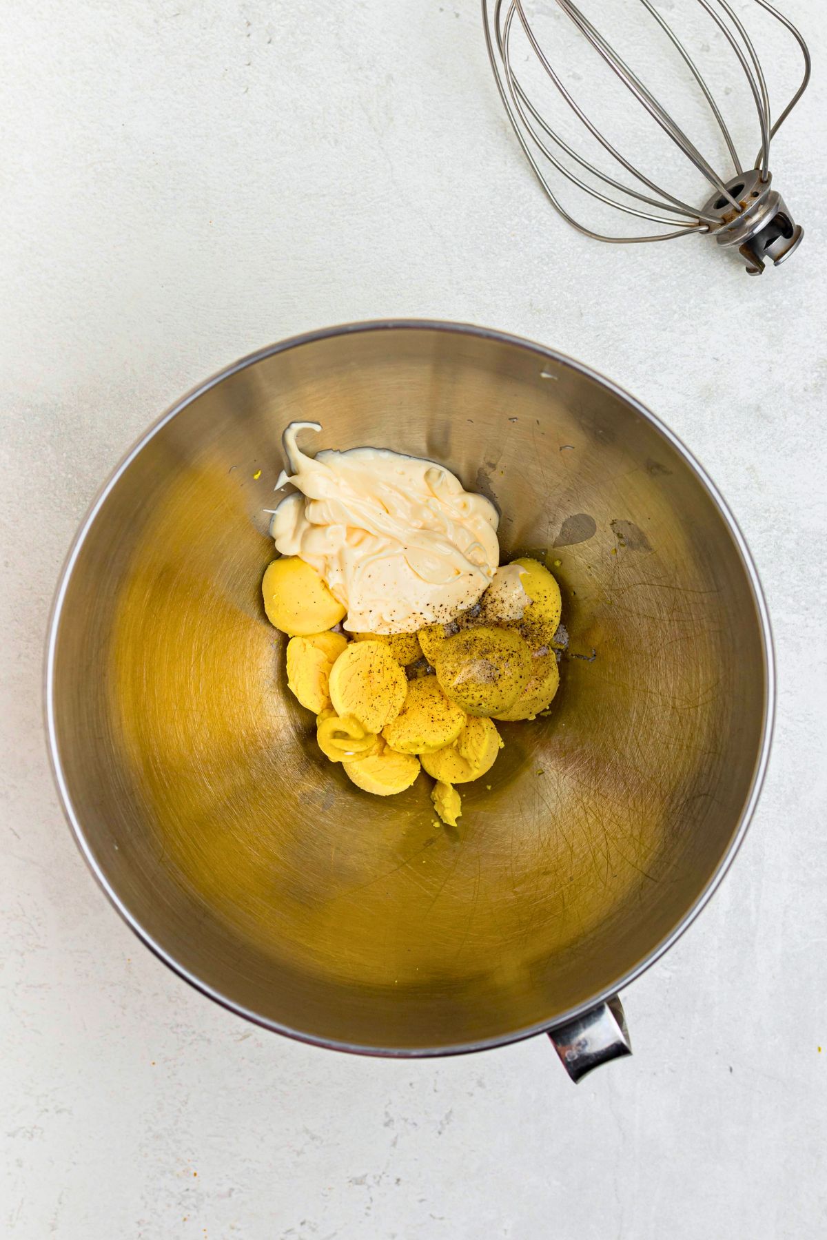 Egg yolks, mustard, mayo, and seasonings, in a silver bowl before mixing.