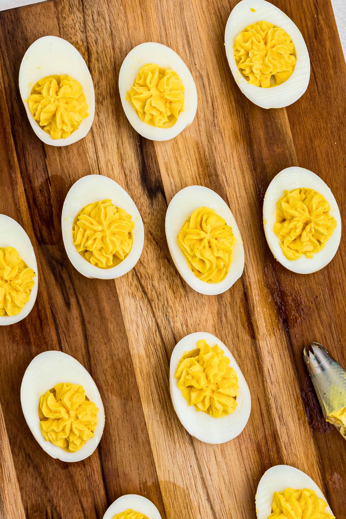 Egg halves piped with yellow yolk mixture to fill center, on a wooden cutting board. 