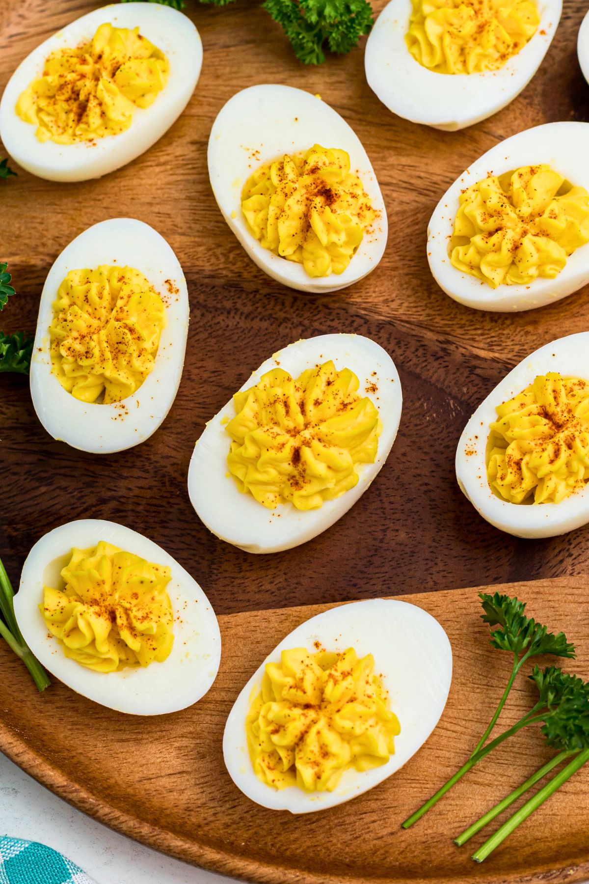 Bright white and yellow deviled eggs, sliced in half, on a round wooden serving platter with parsley garnish.