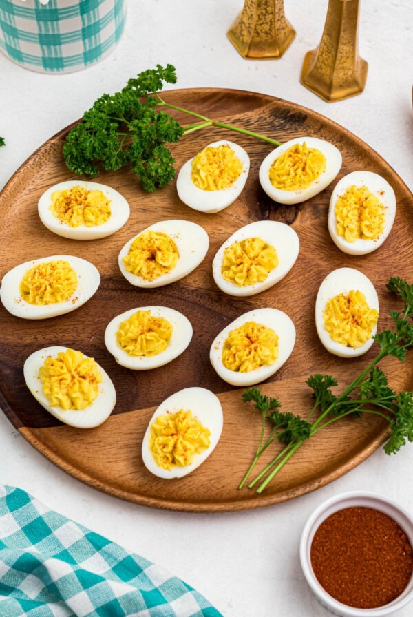 Bright white and yellow deviled eggs, sliced in half, on a round wooden serving platter with parsley garnish.