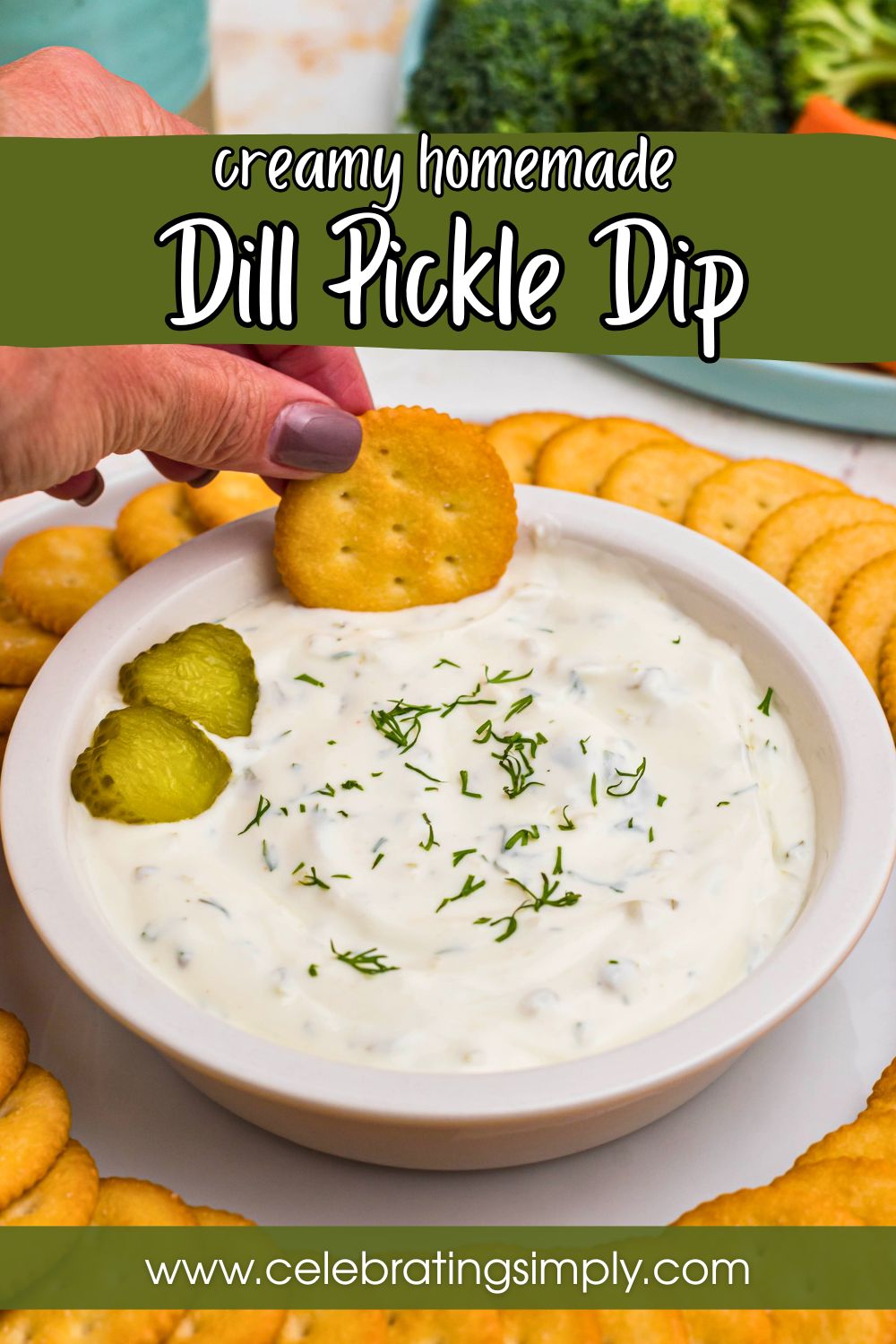 Small white bowl filled with creamy white dip, topped with slices of pickles, surrounded by round crackers, and a plate of fresh vegetables.
