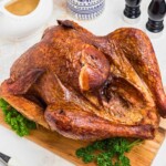 Golden smoked turkey on a brown wooden cutting board, with parsley next to it as a garnish.