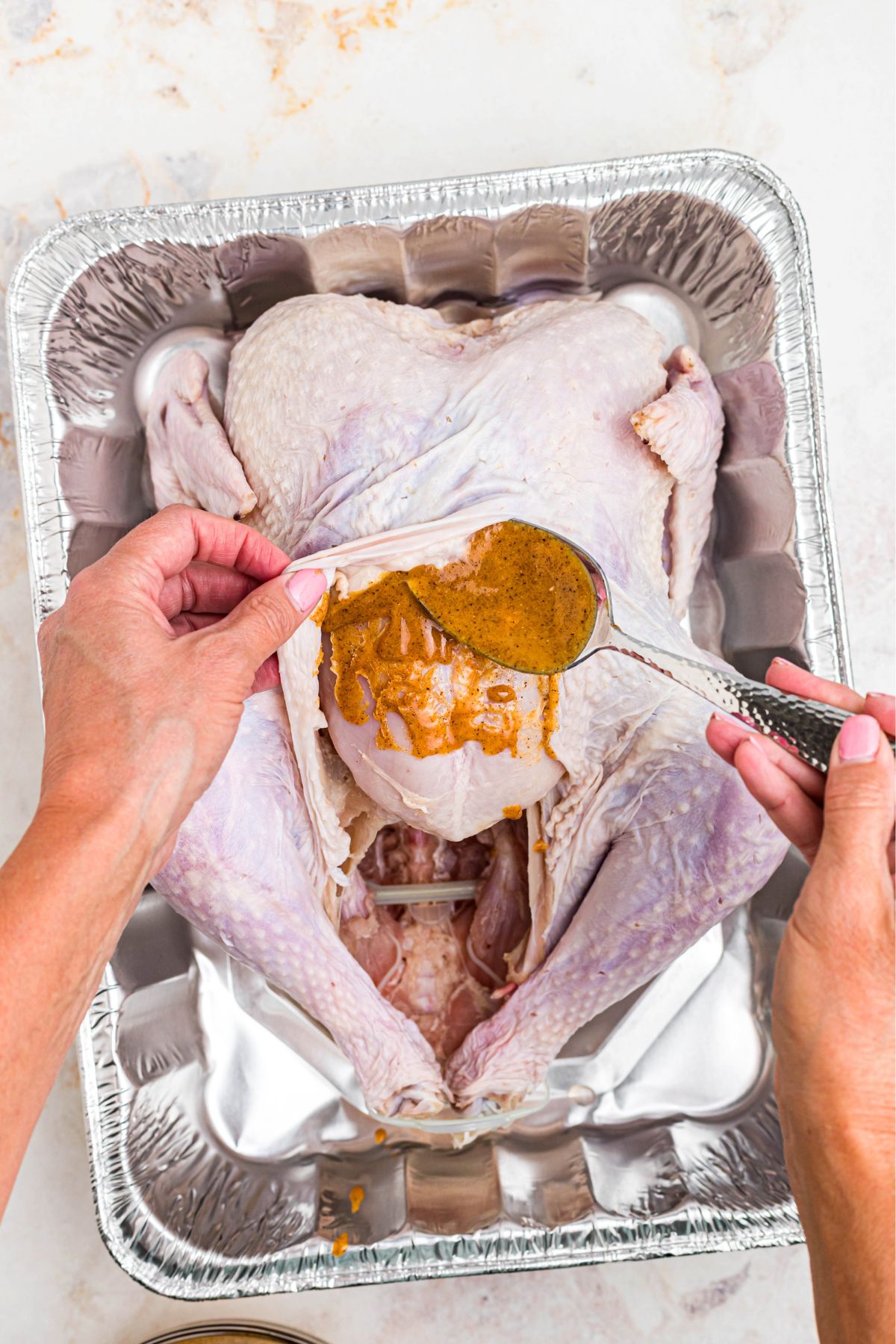 Uncooked turkey with skin lifted being coated with seasoned melted butter before cooking.