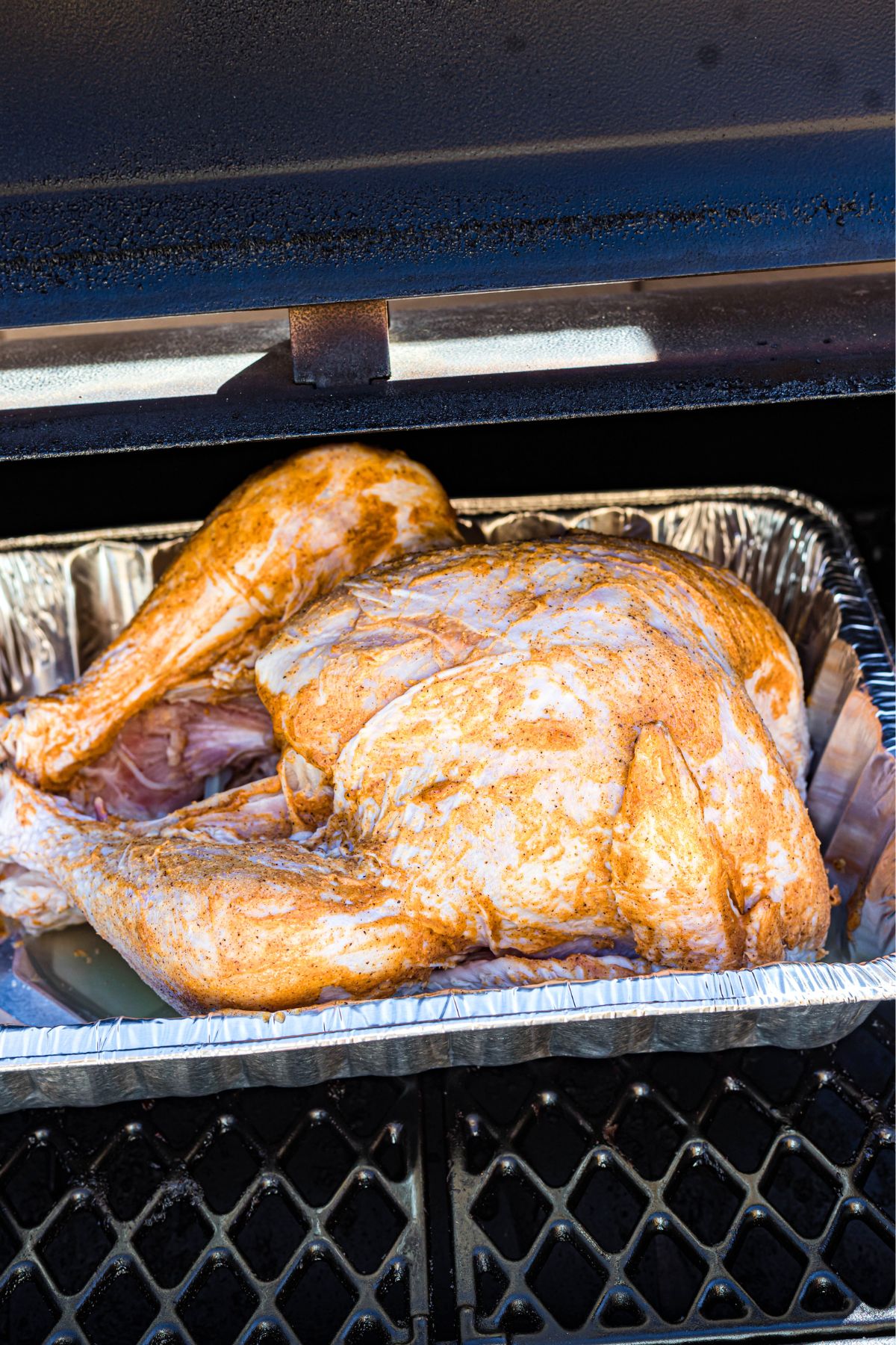 Seasoned uncooked turkey in a roasting pan, placed in the smoker.