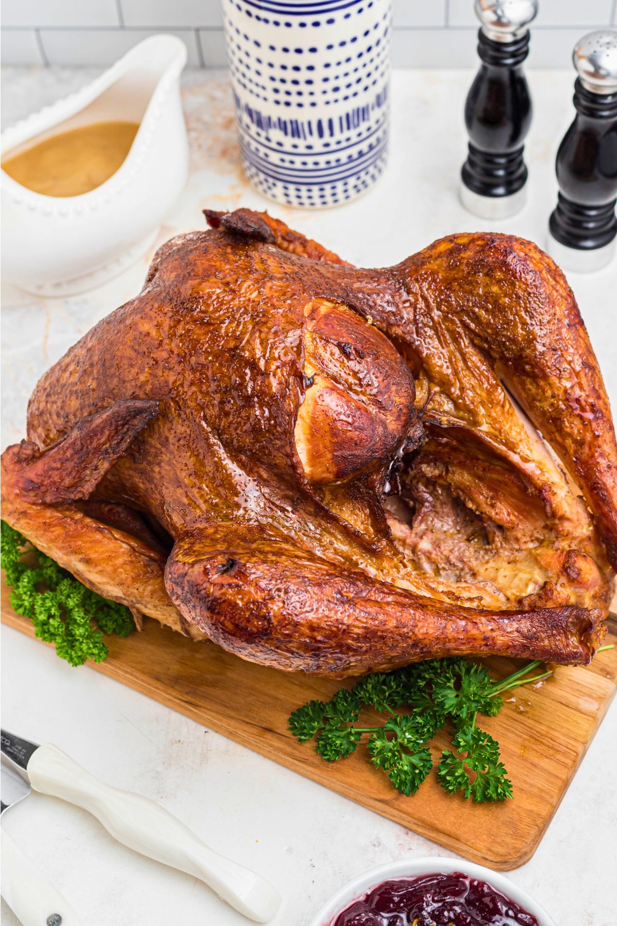 Golden smoked turkey on a brown wooden cutting board, with parsley next to it as a garnish.