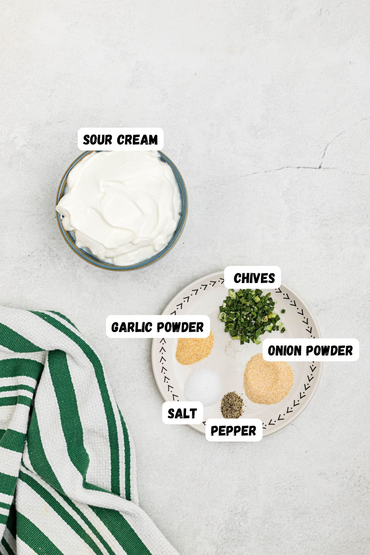 Ingredients needed to make sour cream dip, measured onto small plate and in a bowl, labeled, on a white marble table. 