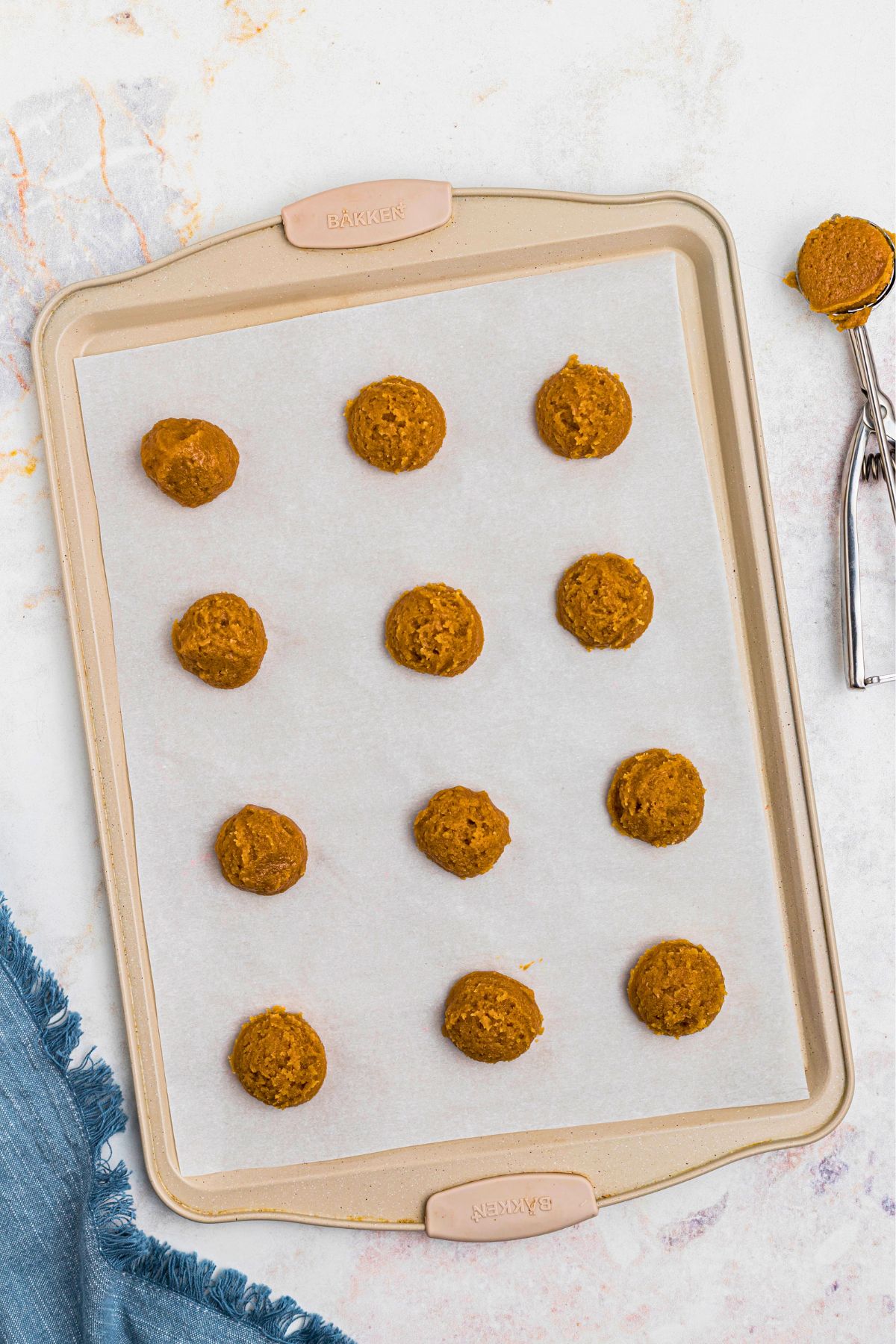 Scoops of cookie dough dropped onto baking sheet, lined with parchment paper, before baking.