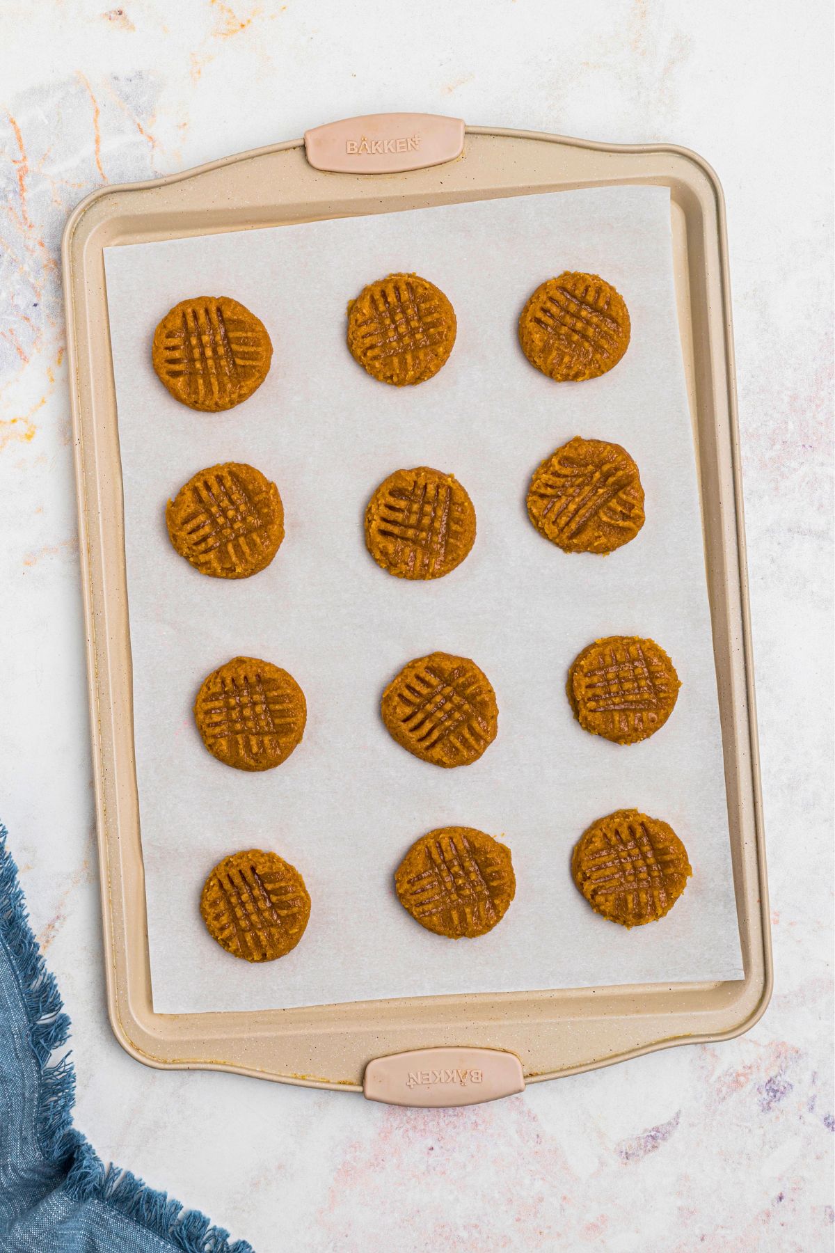 Uncooked balls of cookie dough on parchment paper lined baking sheet, pressed down with a fork to make criss cross shape, before baking. 