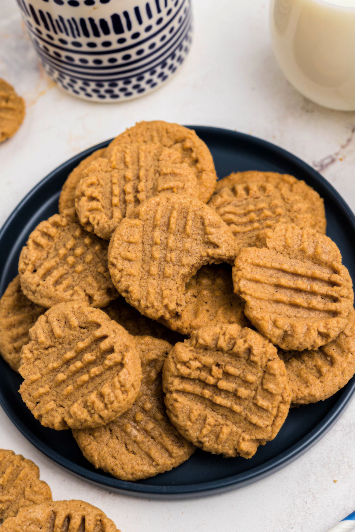 Blue round plate filled with a pile of peanut butter cookies with the top cookie missing a bite. 