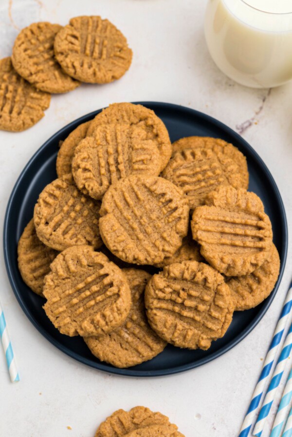 Blue round plate of cookies, surrounded by glasses of milk and blue straws on a marble table.