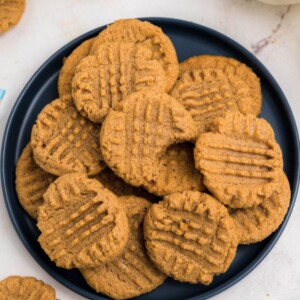 Blue round plate filled with a pile of peanut butter cookies with the top cookie missing a bite.