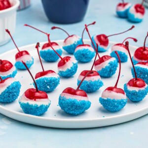 Cherries coated in white chocolate, then dipped in blue sanding sugar, on a white round plate.