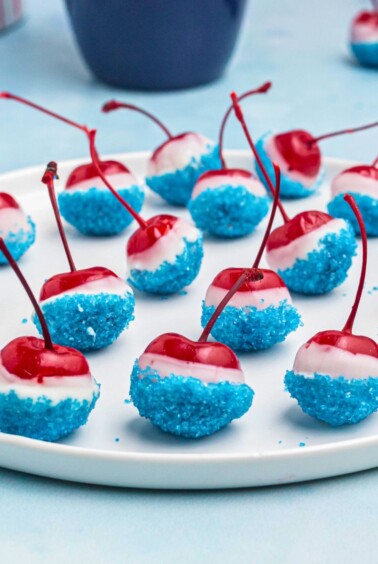 Cherries coated in white chocolate, then dipped in blue sanding sugar, on a white round plate.
