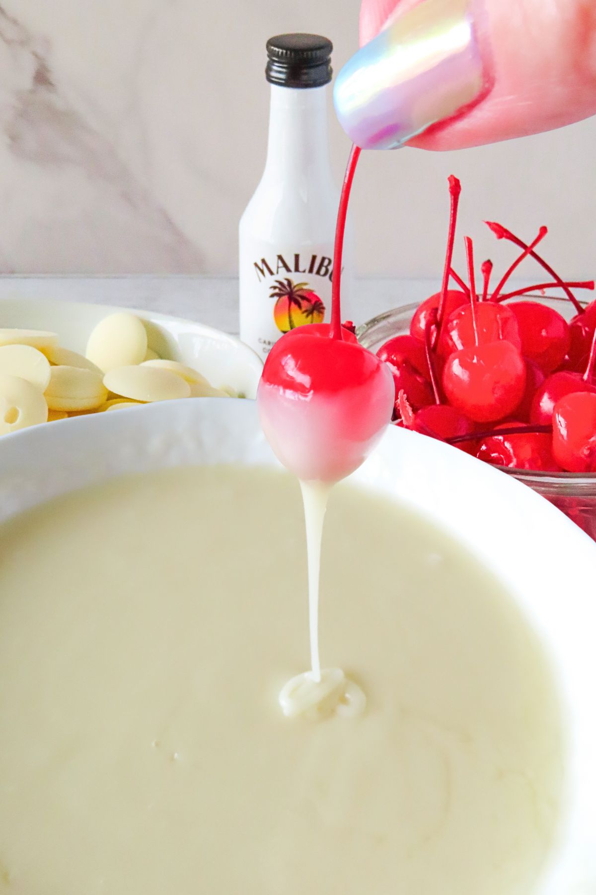 Bright red cherry being dipped into white melting chocolates. 