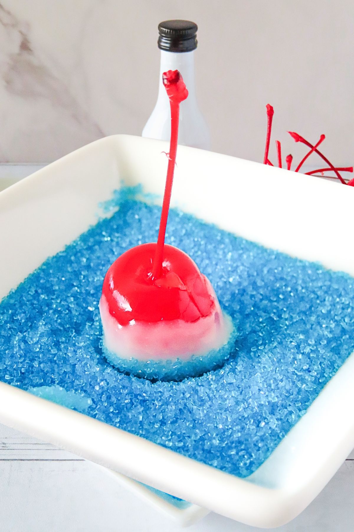 Red cherry with a stem, coated in white chocolate, then dipped into blue sanding sugar. 