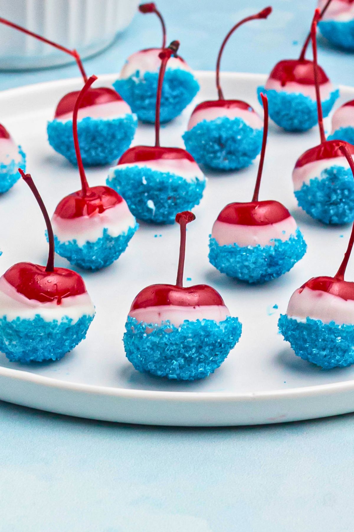 Cherries coated in white chocolate, then dipped in blue sanding sugar, on a white round plate. 