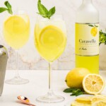 Glass of yellow limoncello spritz, topped with a sprig of mint and a lemon slice garnish.