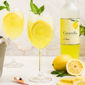 Glass of yellow limoncello spritz, topped with a sprig of mint and a lemon slice garnish.