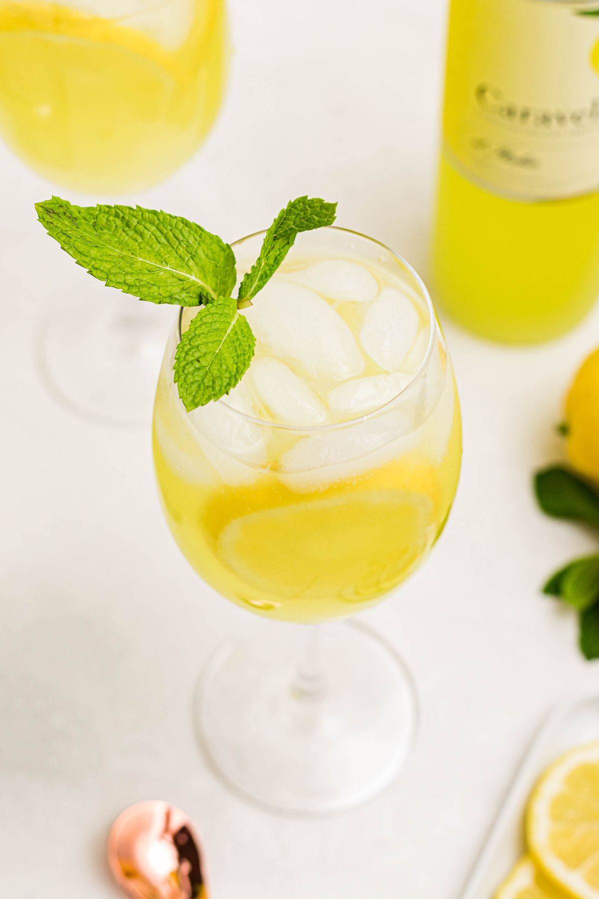 Image of wine glass filled with spritz ingredients, topped with sprig of mint, on a white marble table. 