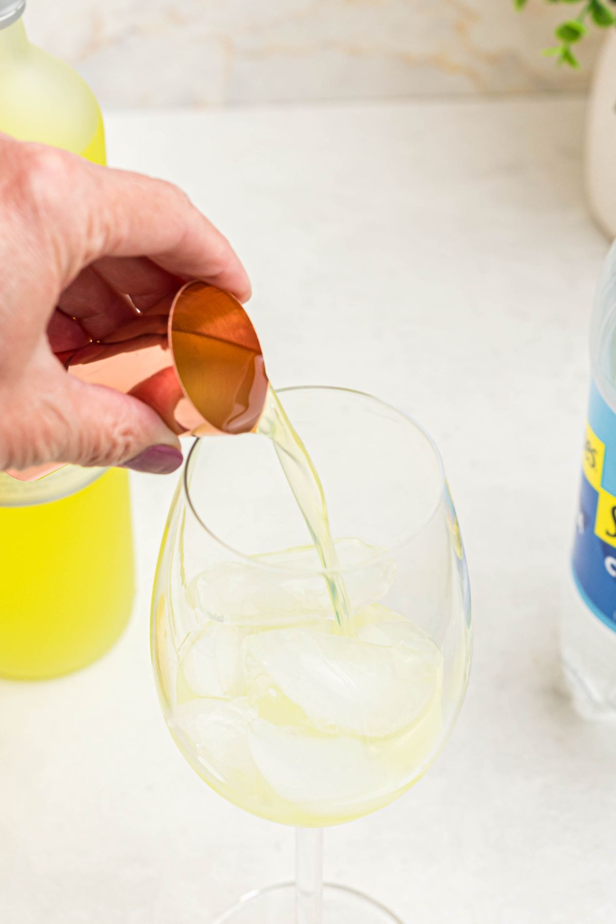 Limoncello being measured and poured into tall wine glass filled with ice. 
