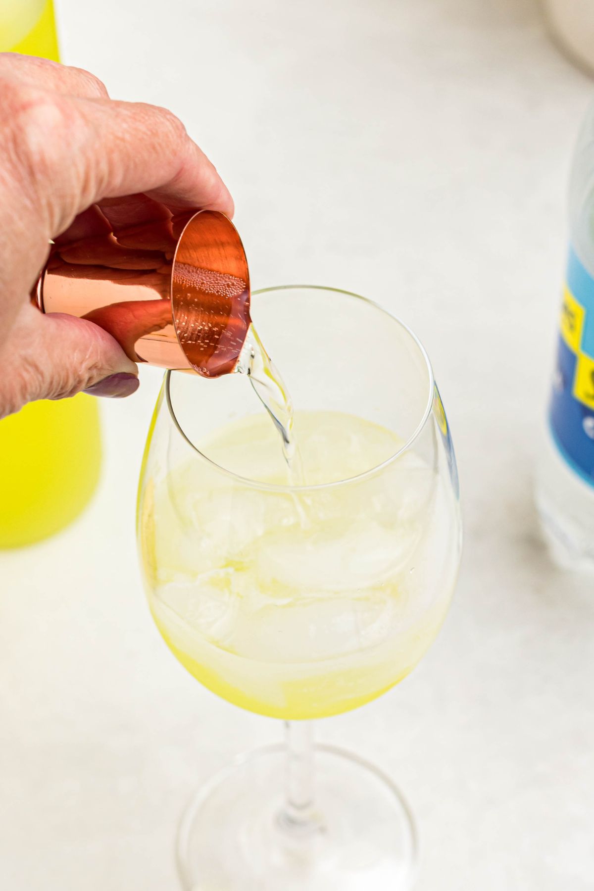Mixing soda water and prosecco with limoncello in clear wine glass. 