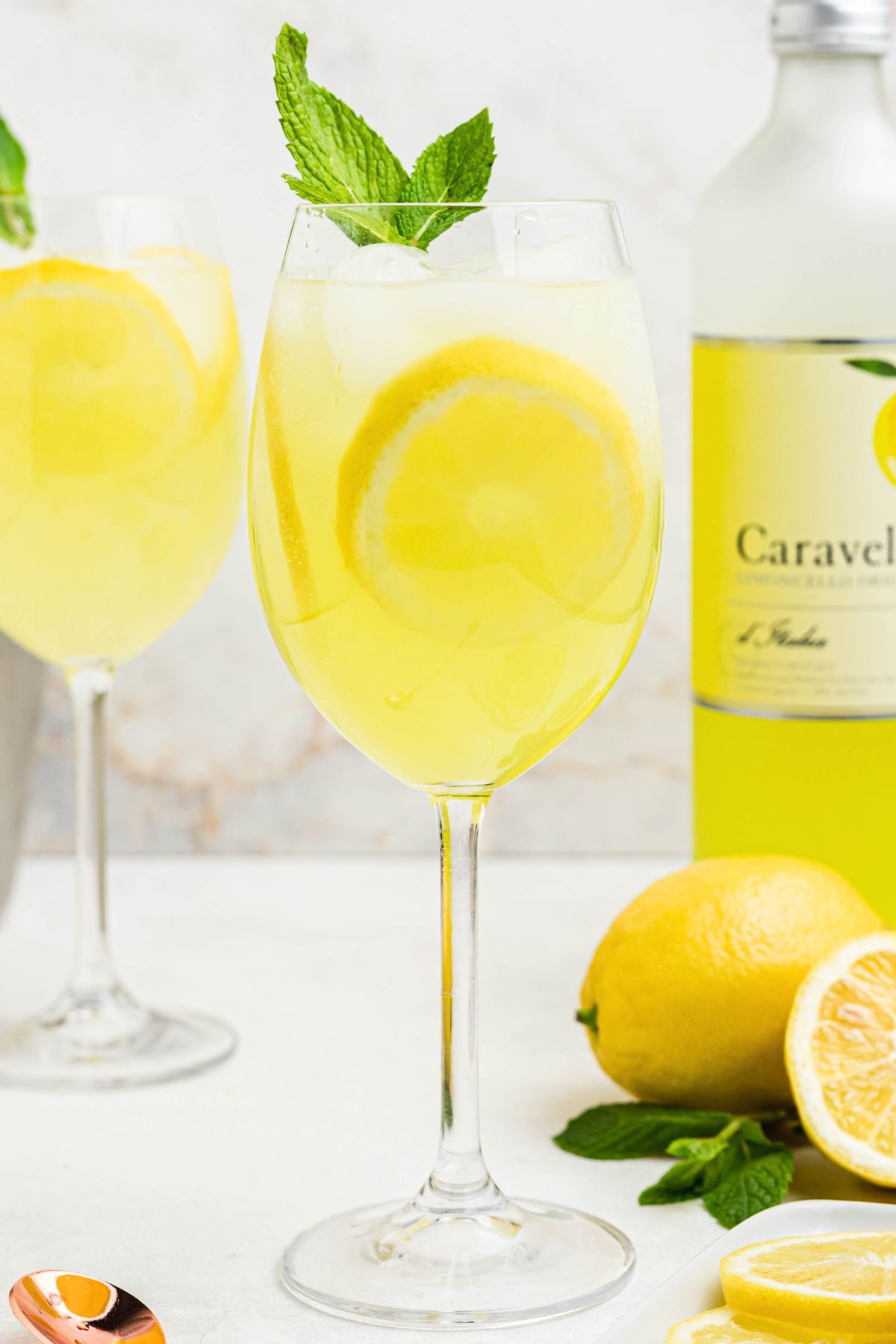 Glass of yellow limoncello spritz, topped with a sprig of mint and a lemon slice garnish.