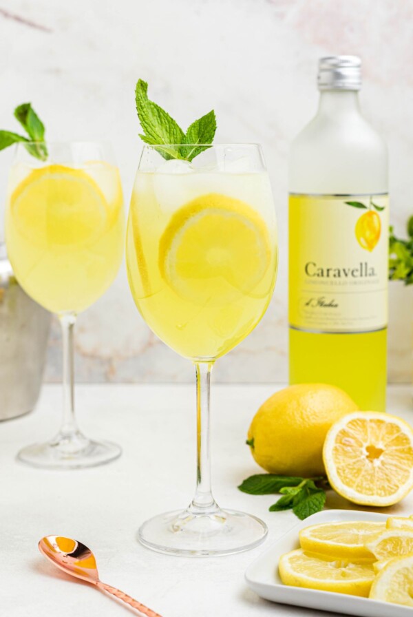 Glass of yellow limoncello spritz, topped with a sprig of mint and a lemon slice garnish.
