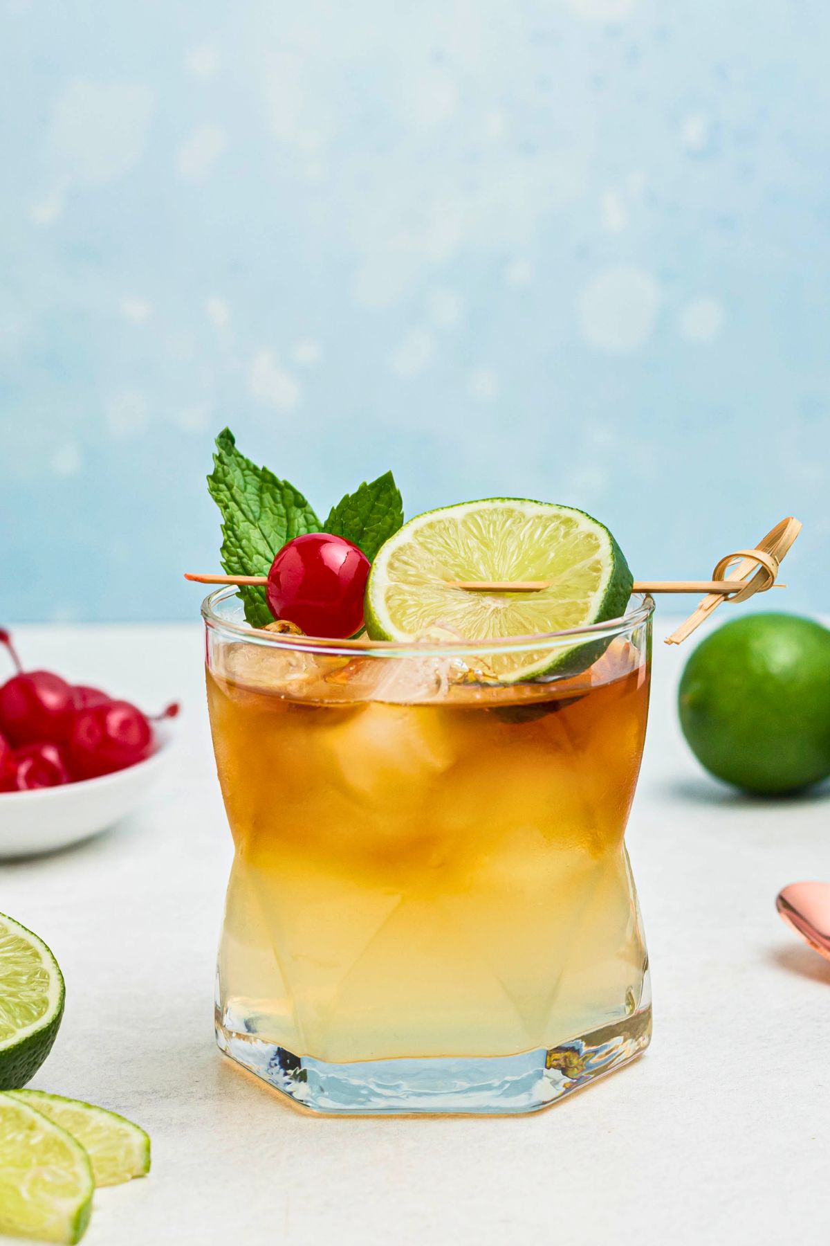 Rum and other ingredients, mixed together to make a Mai Tai, in a clear half glass, topped with a cherry and lime slice as a garnish.