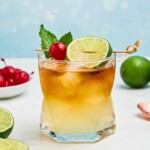 Rum and other ingredients, mixed together to make a Mai Tai, in a clear half glass, topped with a cherry and lime slice as a garnish.