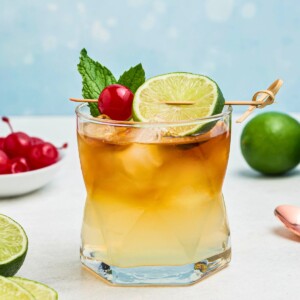Rum and other ingredients, mixed together to make a Mai Tai, in a clear half glass, topped with a cherry and lime slice as a garnish.