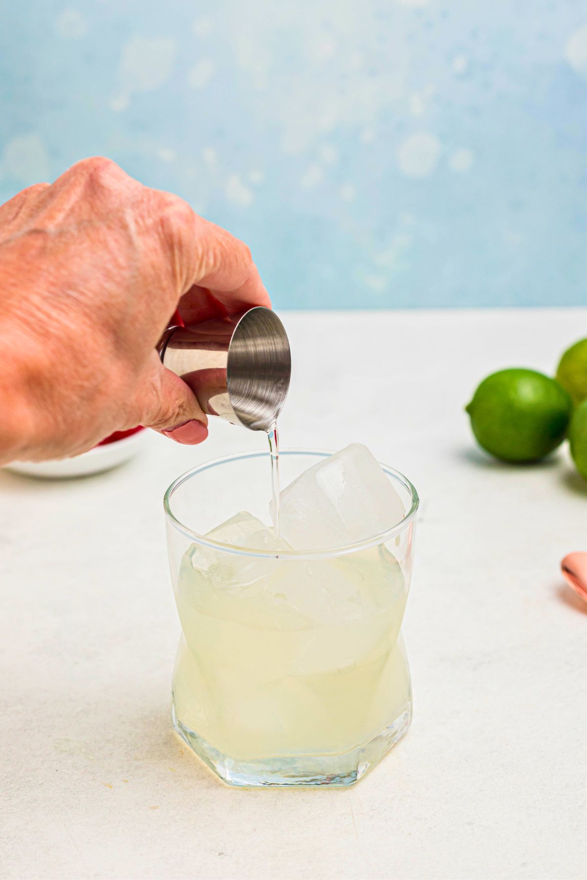 Clear liquid being poured into a clear glass, filled with ice. 