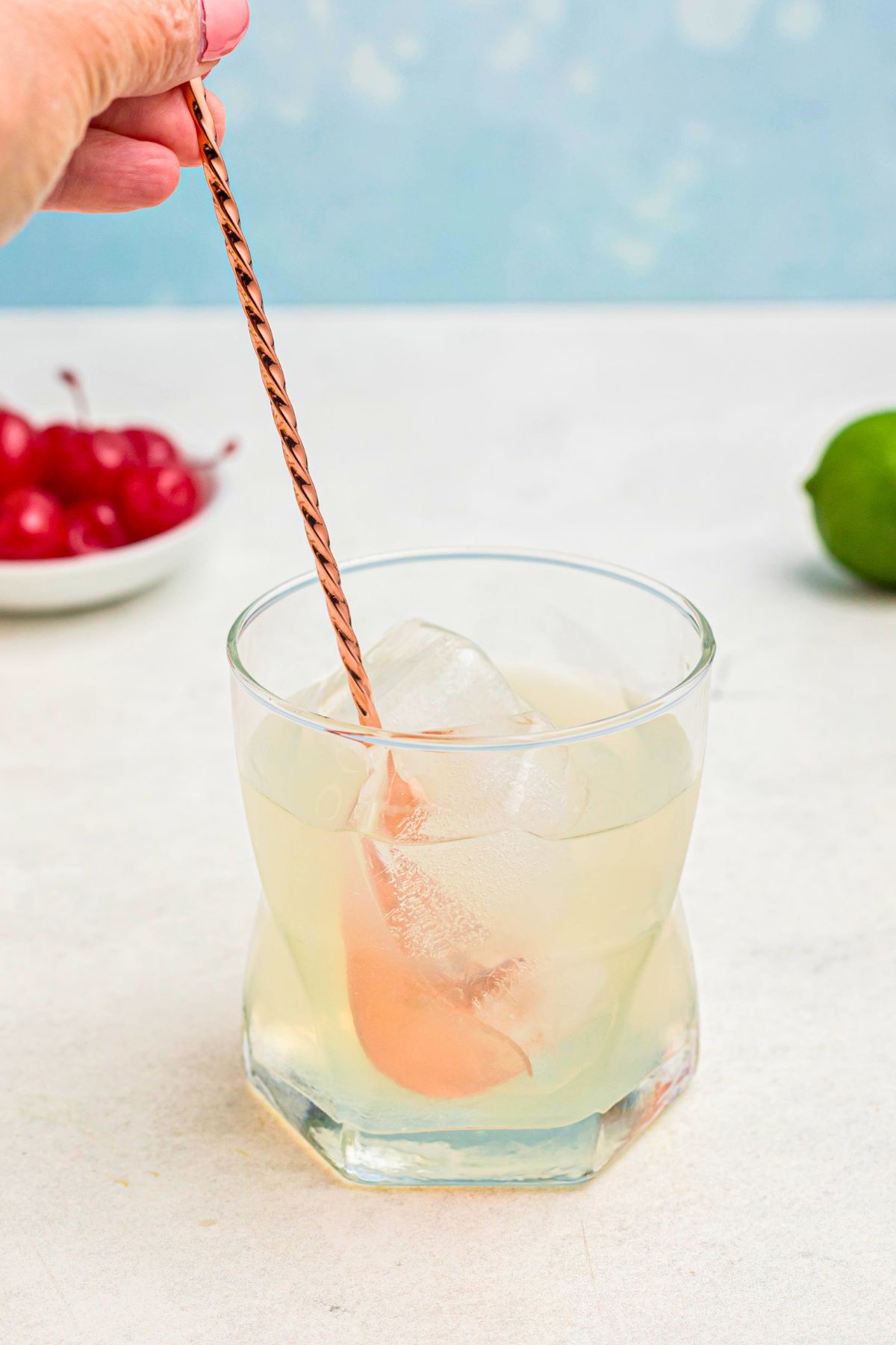 Ingredients in a clear glass are being stirred together with a rose gold spoon. 