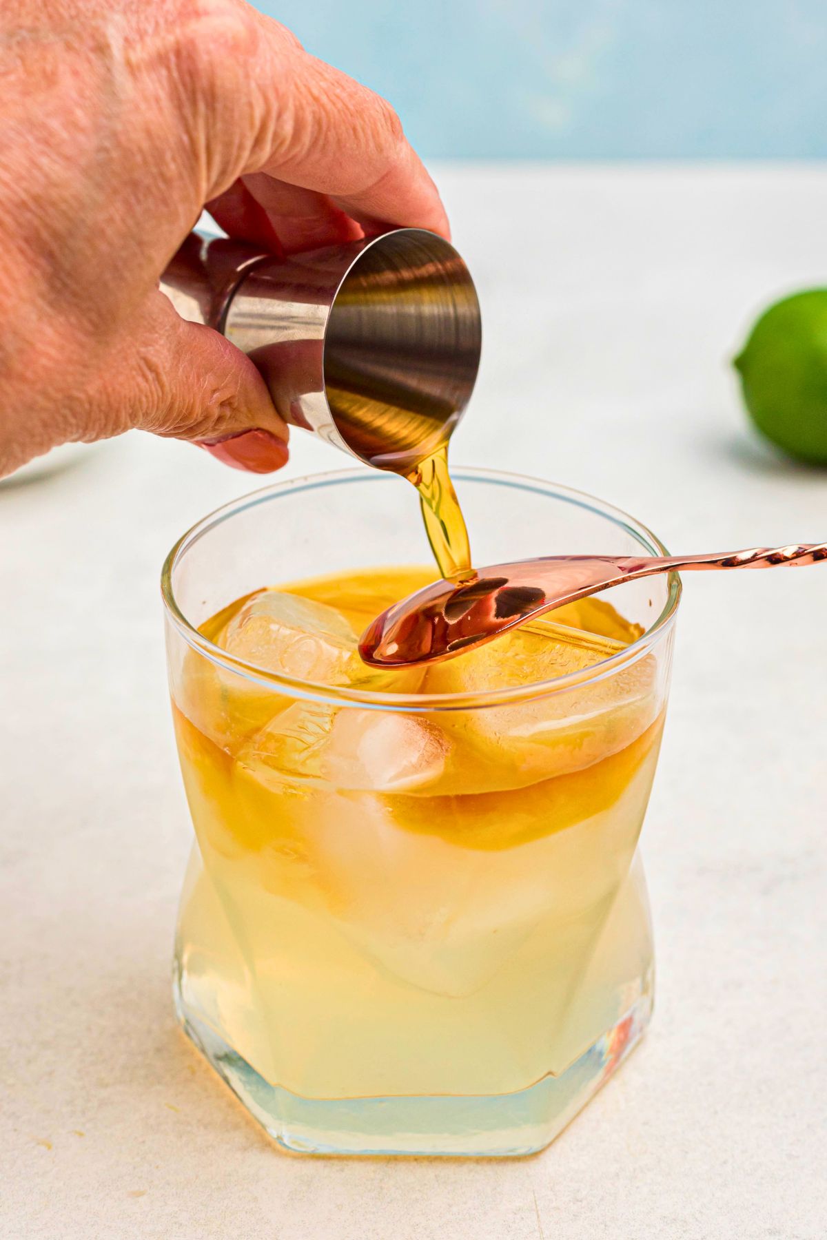 Dark rum being poured over the back of a spoon to create a layer effect in a mai tai, in a clear glass. 