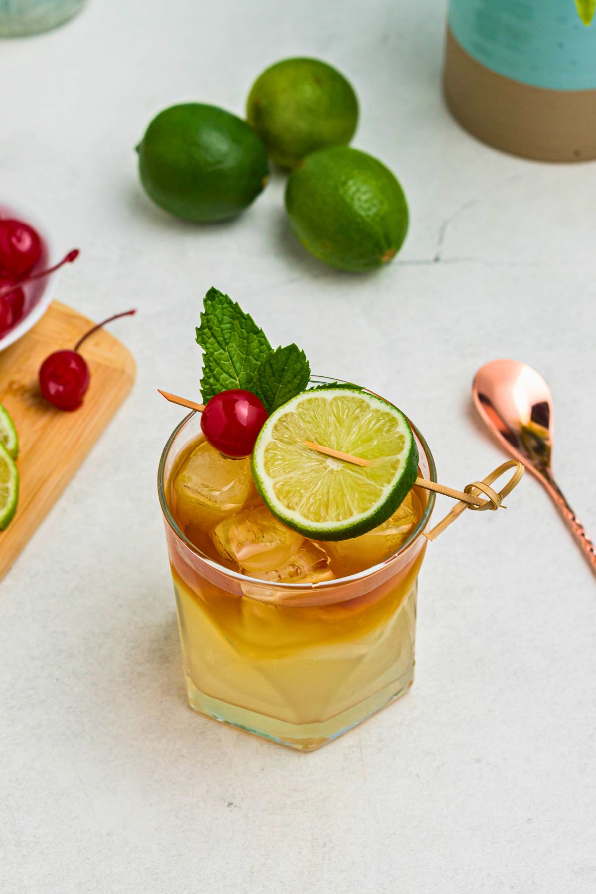 Overhead image of rum and other ingredients, mixed together to make a Mai Tai, in a clear half glass, topped with a cherry and lime slice as a garnish.