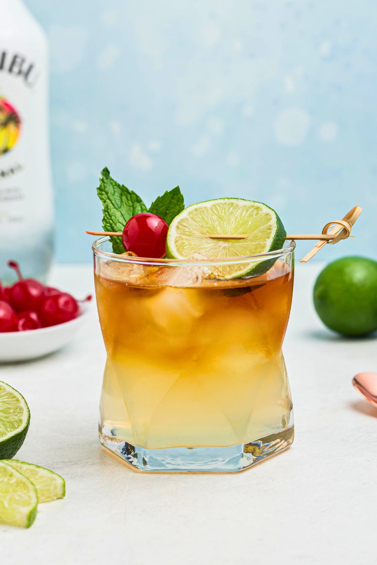 Rum and other ingredients, mixed together to make a Mai Tai, in a clear half glass, topped with a cherry and lime slice as a garnish. 
