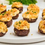 Brown mushrooms topped with cream cheese mixture and breadcrumbs, on a white plate.