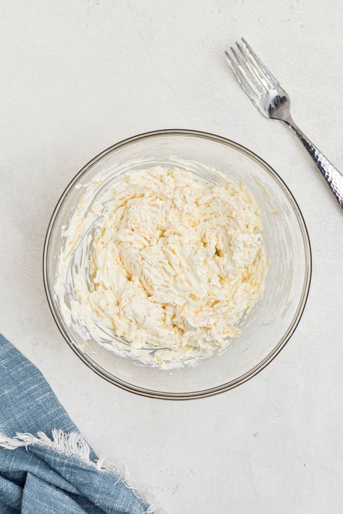 Medium clear glass bowl with cream cheese, parmesan cheese, and other ingredients, mixed together. 