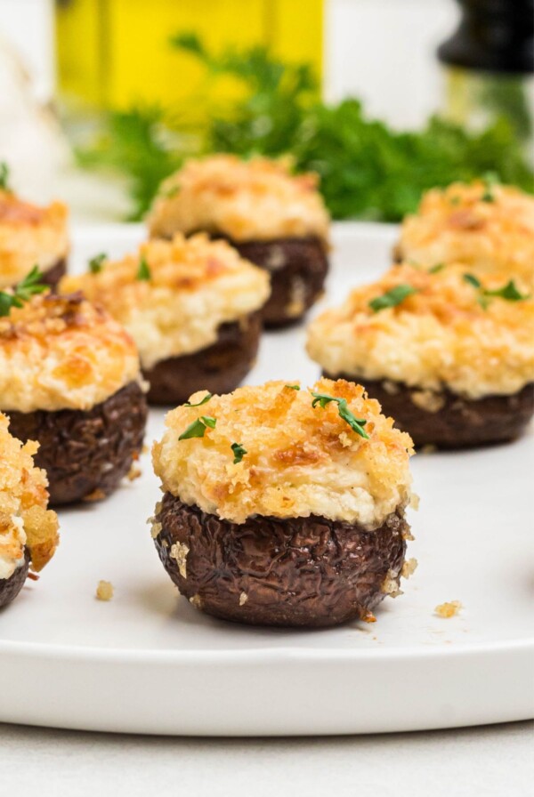 Brown mushrooms topped with cream cheese mixture and breadcrumbs, on a white plate.