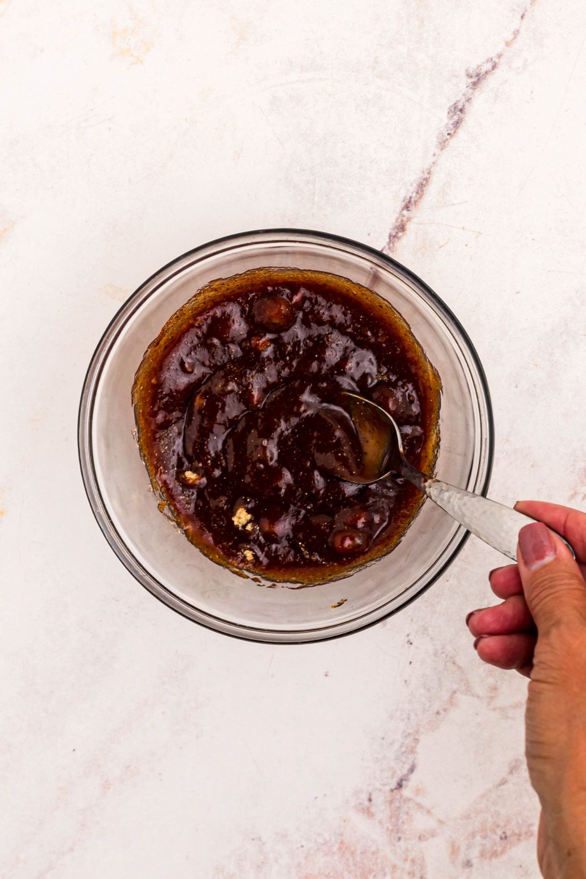 BBQ sauce, brown sugar, and spices, mixed together in a clear glass bowl. 