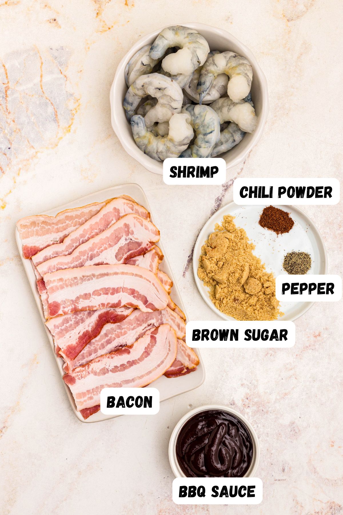 Ingredients measured and labeled, needed to make bacon wrapped shrimp, on a marble table. 