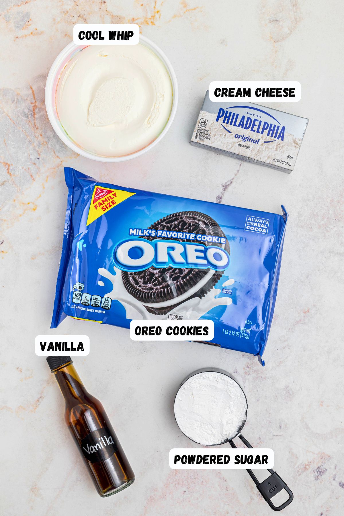 Oreos, powdered sugar, vanilla, cream cheese, and cool whip, on a white marble table. 