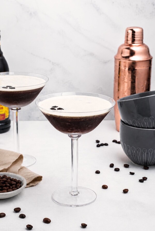 Martini glass with coffee and vodka mixture, with a frothy foam on top, on a marble table with coffee beans scattered.