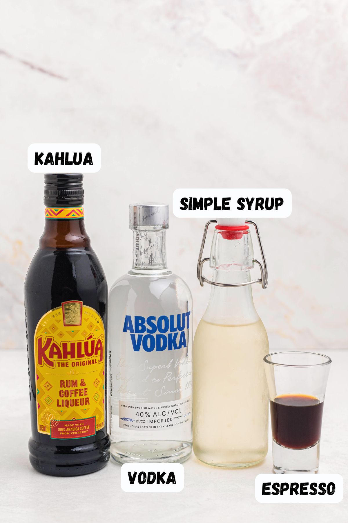 Kahlua, vodka, simple syrup, and espresso, on a white marble table, labeled. 