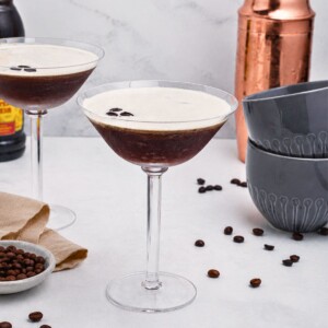 Martini glass with coffee and vodka mixture, with a frothy foam on top, on a marble table with coffee beans scattered.