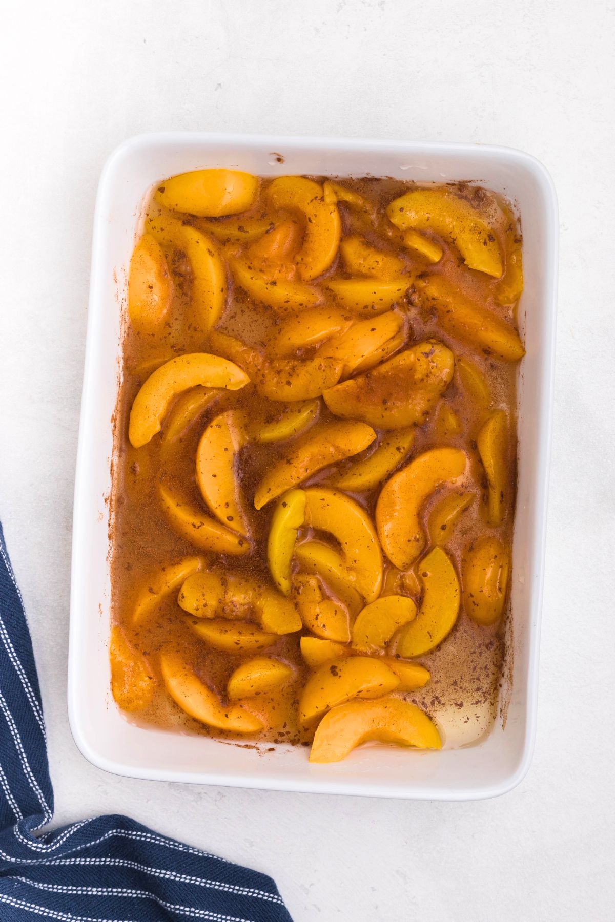 White rectangle dish filled with peaches, mixed with cinnamon and vanilla. 